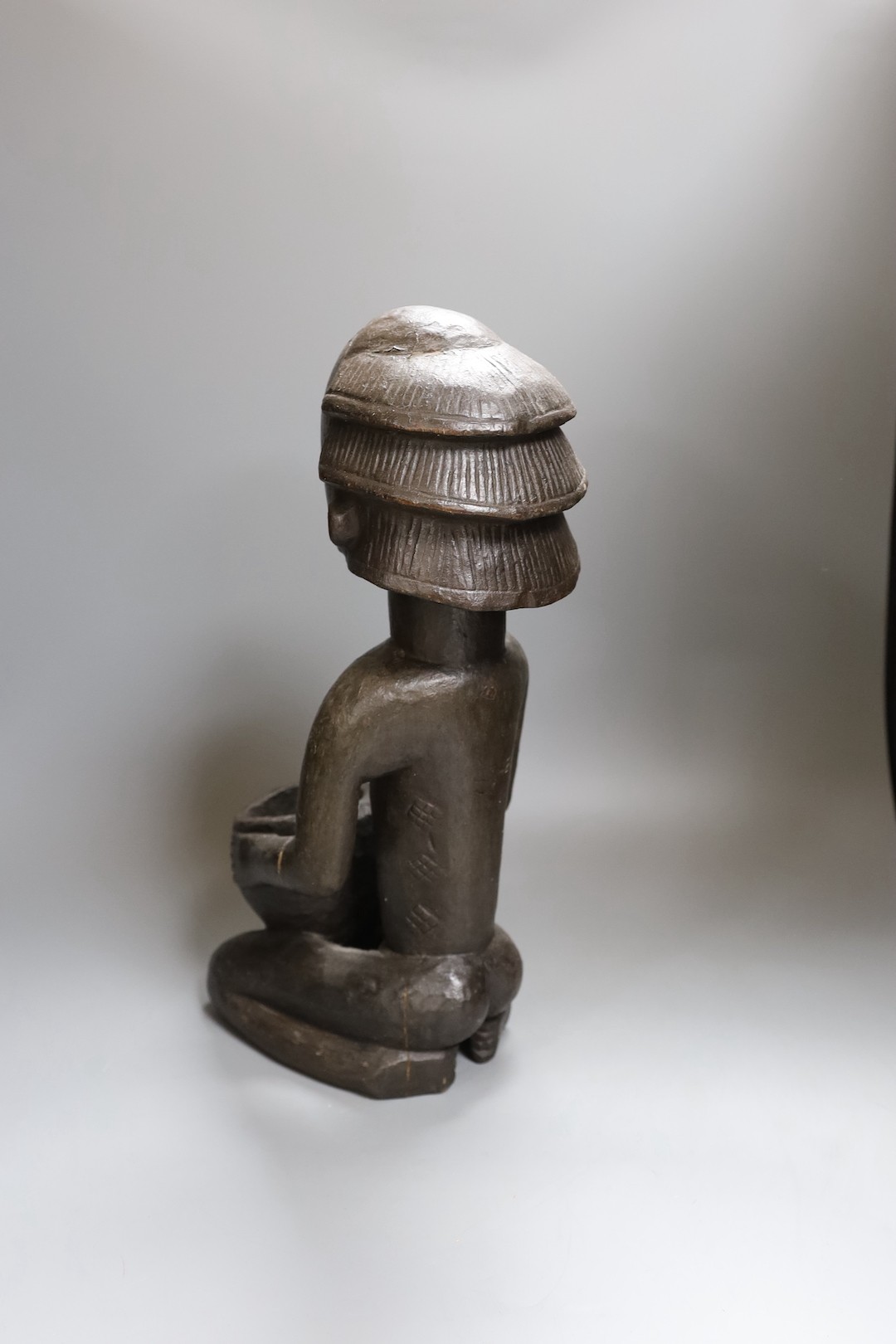 An African tribal carved wood kneeling figure holding bowl (44cm high) and tribal hand instrument (2)